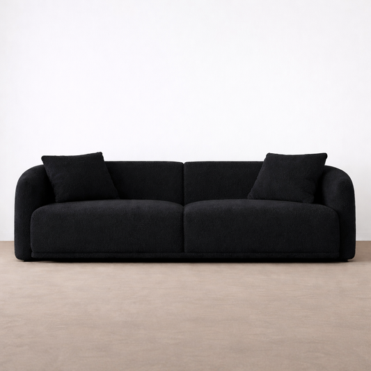 Black sofa with two cushions on a beige floor and white wall background