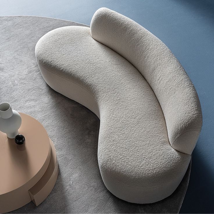 Curved, textured sofa against a blue wall with a small round table and white vase.